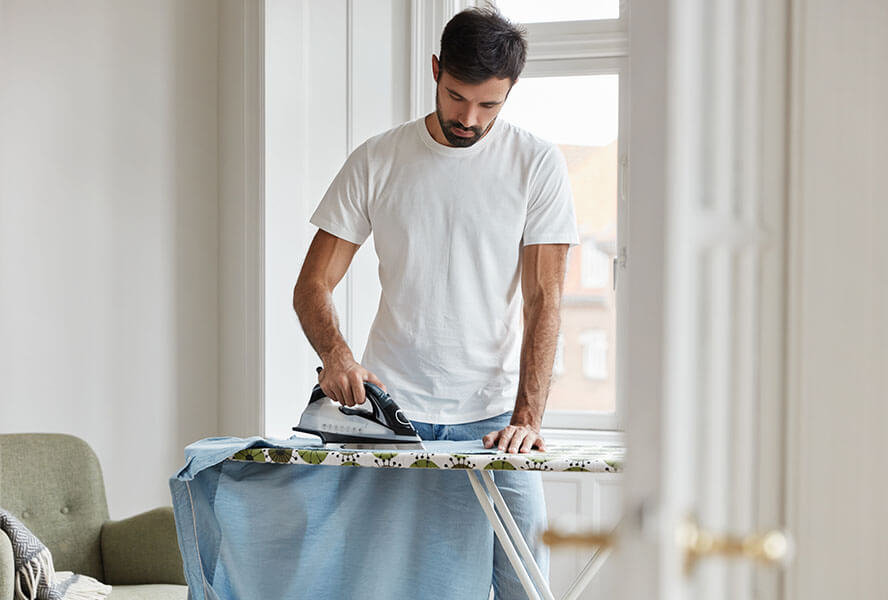 Mann in einem hellen Shirt bügelt sein weißes Hemd