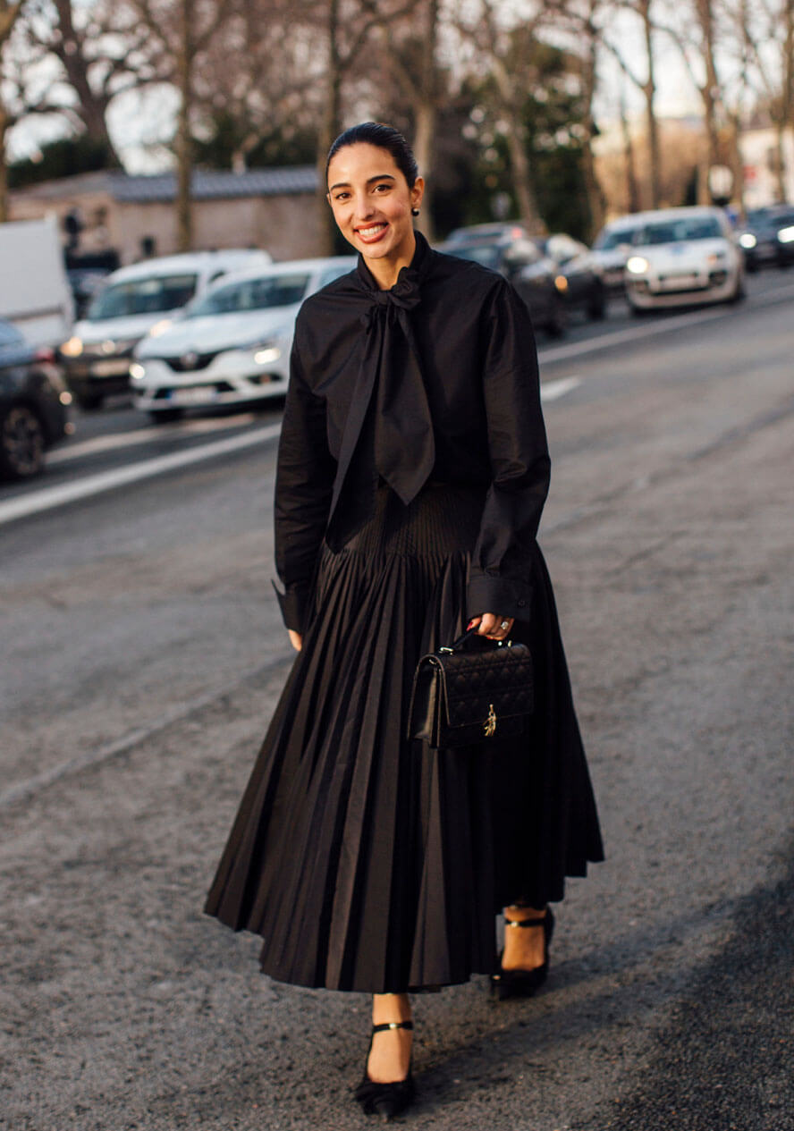 Frau trägt ein schickes Business-Outfit und kombiniert zu einem schwazen Plisseerock eine schwarze Bluse