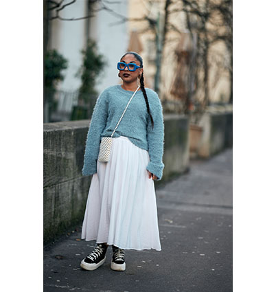 Frau in einem weissen Plisseerock und blauen Pullover trägt Sneaker